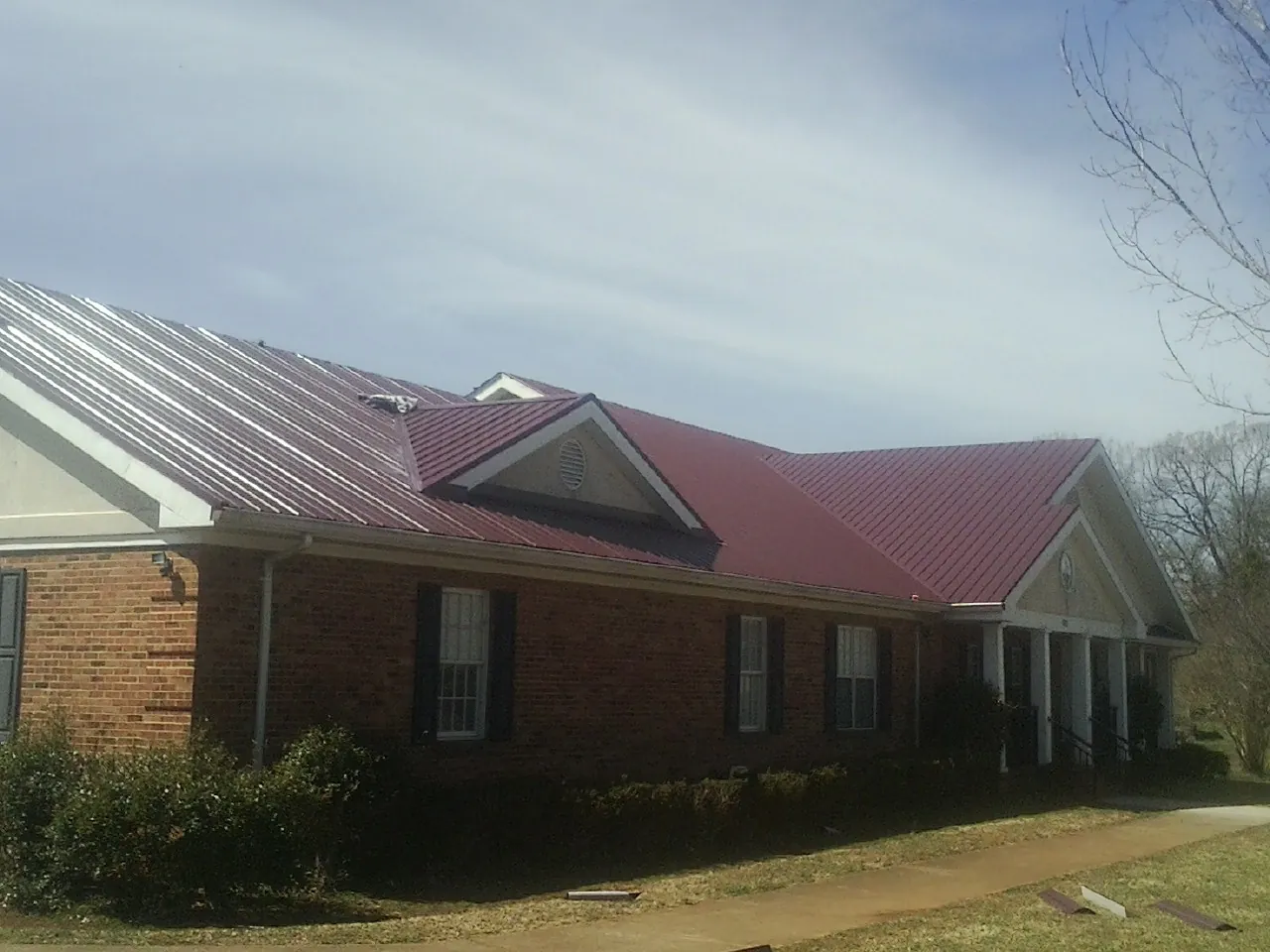 Red metal roof with gabled entries on a long brick building, from a Hail Damage Roof Repair job in Bryantown